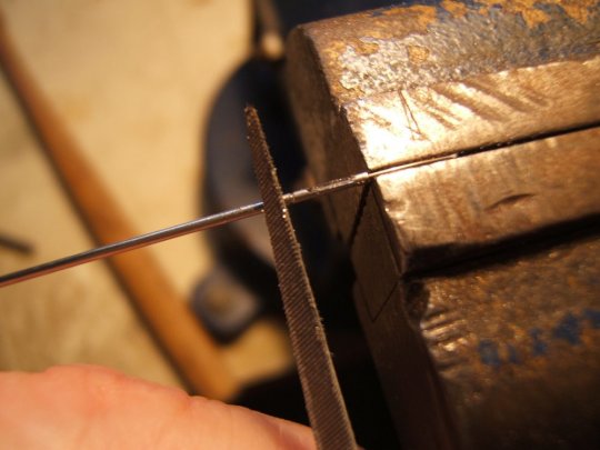 Den Stahldraht im Schraubstock einspannen und dann bei langsamer Drehung der Kanüle mit einer Dreikantfeile ringsum eine feine Kerbe feilen. Die Kerbe muss nicht bis auf den Stahldraht gefeilt werden, so dass man sich die Feile ruinieren würde.